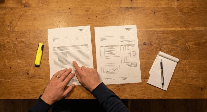 Twee bouwoffertes naast elkaar op tafel terwijl iemand de prijzen vergelijkt met een markeerstift